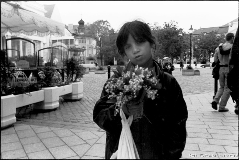 1999.06 Gypsy girl in Bratislava_hf <div align=left>June 1999<br>A long weekend and a bouncy over-night train-ride to Bratislava (NB. check your visa requirements carefully or you might be detained in a border village police station!...) Slovakia is only a short distance from Serbia. A gypsy girl is selling flowers while an anti-NATO demonstration is taking place in the square behind me, and the graffiti draws parallels between Clinton and Hitler. (I wonder about her future?) This, in stark contrast to Paris where I saw the same words on the wall, but for Milosevic. <br>Having a war on ones doorstep is a thought-provoking eye-opener...a weighty matter not lost on anyone here in Germany, but with no clear solutions yet in sight. Someone said, "The more things change, the more they remain the same." <br>Meanwhile, I have to work on, and photograph. Summer is here, and more travelling is planned. Maybe Ill write you something lighter about Paris next month. <br>Dean<br>