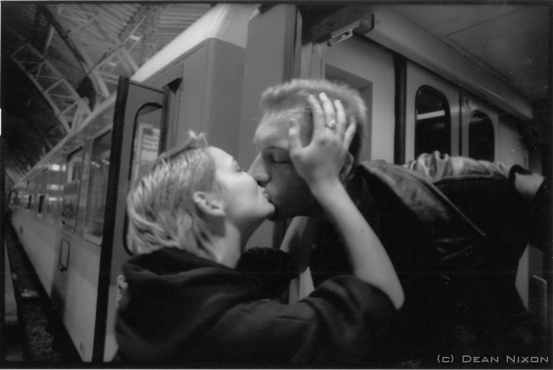 1999.08 Kiss. Leipzig_hf <div align=left>August 1999<br>Ok, Ill accept that it doesnt quite measure up to Doisneaus "Kiss", but Ill guarantee that it wasnt posed. In fact I only had seconds to set my exposure and distance when I saw this reflected in the window of a train at the next platform...spun around and got just one shot (OM 1, 24mm, F 2.8 @ 1/15, TMAX 400) <br>But it was also a reminder of the occasional difficulties of pointing cameras at people in public places. Some East-europeans are still a bit uncomfortable about this and will turn aside, cover their faces, or even object loudly. <br>Once, I was with a politician in a public gallery and was pounced on by a zealous security guard when my trusty (& rusty) XA emerged for a perfectly innocent snap "...verboten...etc" despite my protestations, and he proceeded to follow us throughout the gallery, literally peeking from corners and ducking out of sight if I looked back at him (all in the best B-grade cold war movie tradition). I was told that he was most probably one of the many "watchers" left over from the old regime here. <br>Ive just purchased a Konica Hexar (not having the extra zero to make it a Leica)...but by all accounts the lens is superb, and it does quite fit the bill for street photography. Maybe a report on that later. <br>Meanwhile Summer continues to be beautiful, though I sometimes miss the mountains and the sea. <br>Tschss, <br>Dean<br>