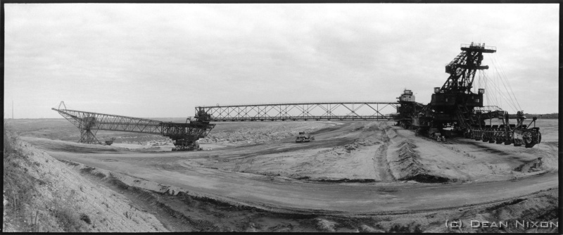 2003.04 Foederbrucke Zwikau_hf <div align=left>April 2003<br>As we are probably all aware, Germans are really into industrial stuff, so... <br>Here we have what had been the biggest movable machine in the world @ 523m long, in a coal mine in Zwenkau near Leipzig, until they blew it up when the mine recently closed (it was too expensive to keep it as a tourist attraction which surely only Germans would think of doing!)<br>If you really want to know: these contraptions are called "overburden conveyor bridges", and are used to transport the top layers of earth from one side of open cast coal mines to the other so that "bucket wheel or chain excavators" can dig out the soft brown coal called "lignite". With still enough coal in eastern Germany for them to keep going until 2050, its a vital and politically sensitive industry: providing thousands of jobs (unemployment in these areas runs at 25%!), and electricity from the cleanest fossil fuel power plants in the world (a big change from the blacked skies and acid rain of 15 years ago!). Dozens of mines like this exist here, which, when they are exhausted, are recultivated into farmland, parks, forests and lakes. Those mines that are still operating sometimes literally gobble up any villages in their paths (they buy them despite protests and build new "replicas" nearby!)<br>Anyway   Im full on teaching in a mining company near the Polish border in order to restabilise the finances (again!) so that I can get the current photo projects sorted and exhibited, which is why I feel obliged to mention coal mines this month and to "not mention the war" cos Im sick of the "experts and the propaganda.<br>BREAKING NEWS (at least as well as a postcard can manage): Leipzig has just been named as Germanys candidate city to host the 2012 Olympic Games - probably got a fat chance though, but helps put a very special city on the map!<br>Gluck auf,<br>Dean<br>PS, dont believe everything you read, unless I wrote it!<br>